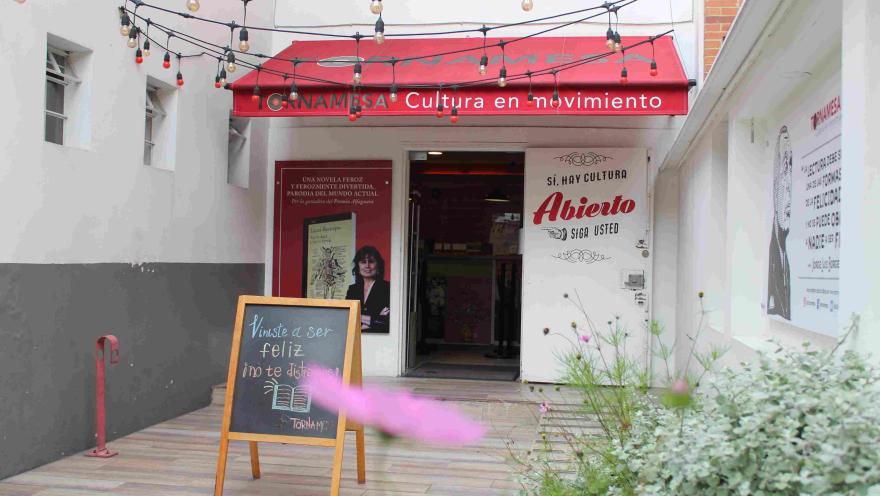 Entrada de la librería Tornamesa con toldo rojo, luces colgantes y un tablero con mensaje en la acera.