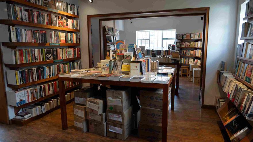 Interior of a bookstore with shelves full of books, a central display table, and boxes of books stacked below.