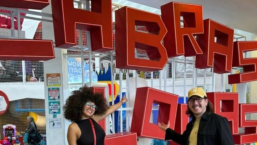 Two people smile and pose in front of large red letters spelling "CABRAS LOCAS" in an indoor play area.