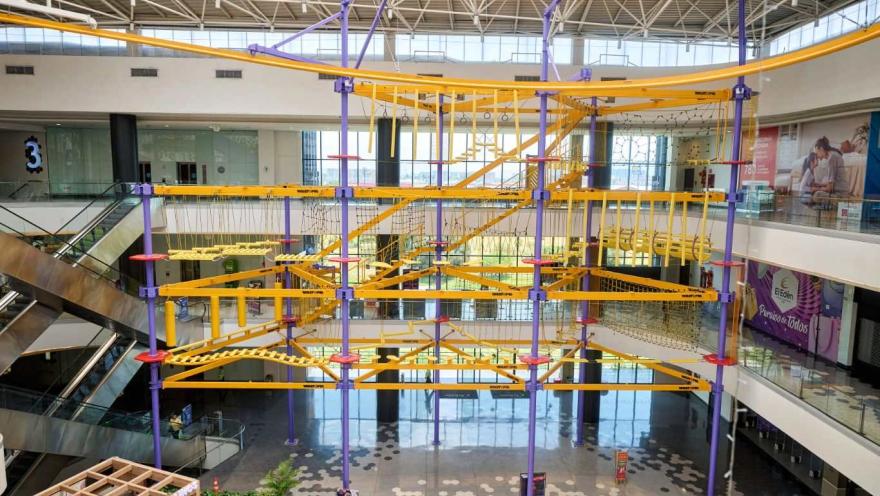 Estructura de circuito de cuerdas y obstáculos suspendidos en varios niveles dentro de un centro comercial amplio y luminoso.