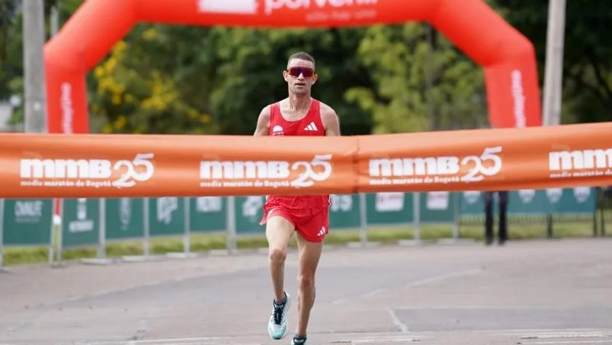 Corredor cruza la meta en solitario durante una carrera, con arco y cinta de llegada al fondo.