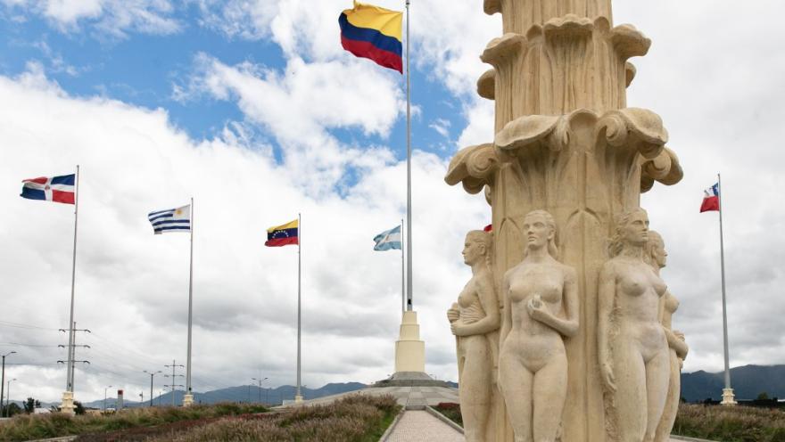 Detalle del Monumento a las Banderas con esculturas de mujeres y banderas ondeando, incluida la de Colombia, bajo cielo nublado.