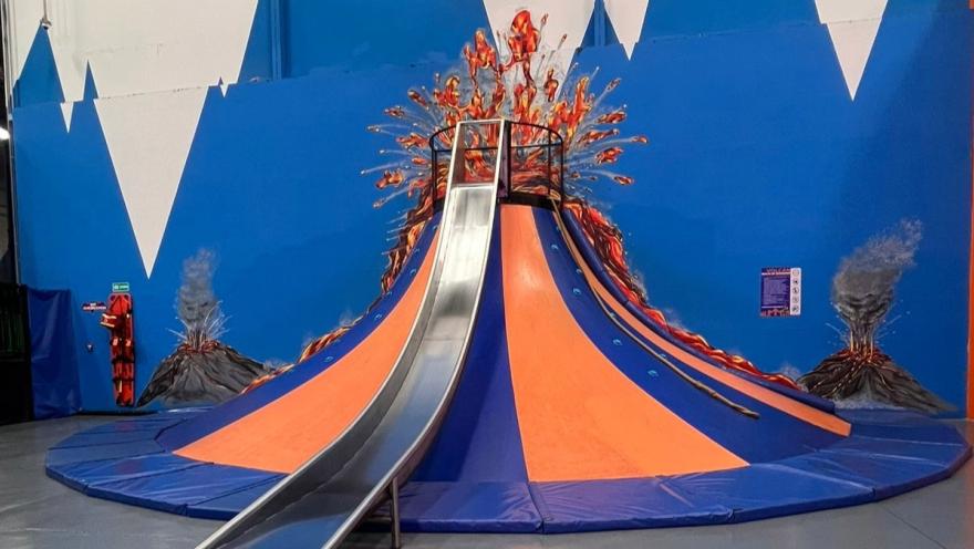  Estructura de juego con forma de volcán en un parque interior, con tobogán central y decoración de erupción en las paredes.