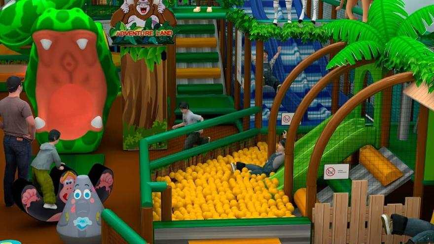  Zona de juegos infantil temática de selva con toboganes, piscina de pelotas y figuras de animales como cebra, león y mono, con niños jugando en el espacio.