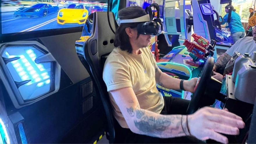 A person uses a virtual reality headset while driving a simulator in an arcade machine with lights and a car display.