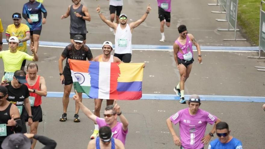  Corredores celebran al cruzar la meta, algunos levantando los brazos y uno sosteniendo una bandera tricolor.