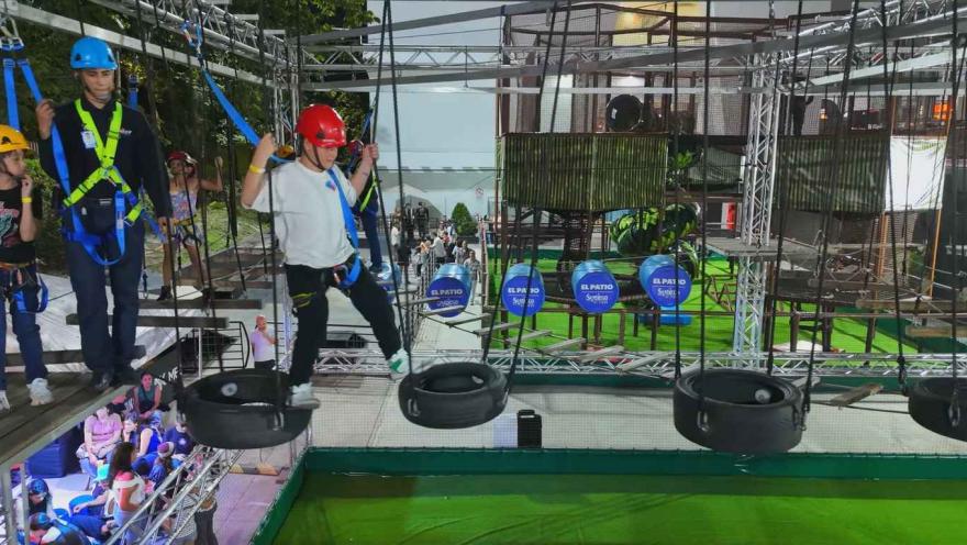 Personas con arnés y casco cruzan un circuito de llantas suspendidas en un parque de aventuras.