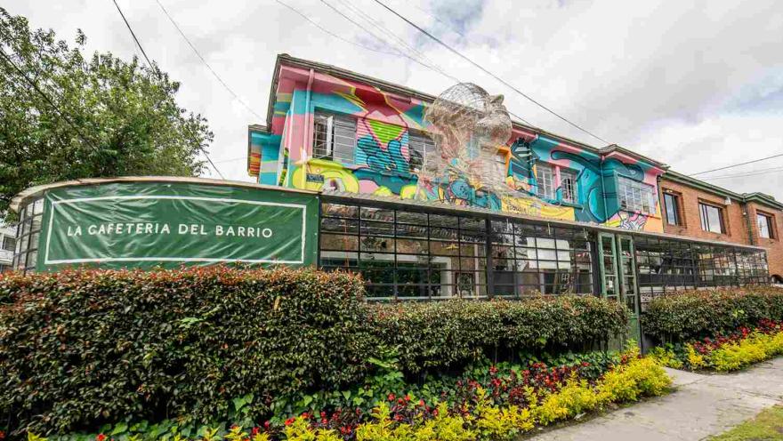 Facade of a neighborhood café with a front garden and a colorful mural on the second floor, combining urban art with traditional architecture.