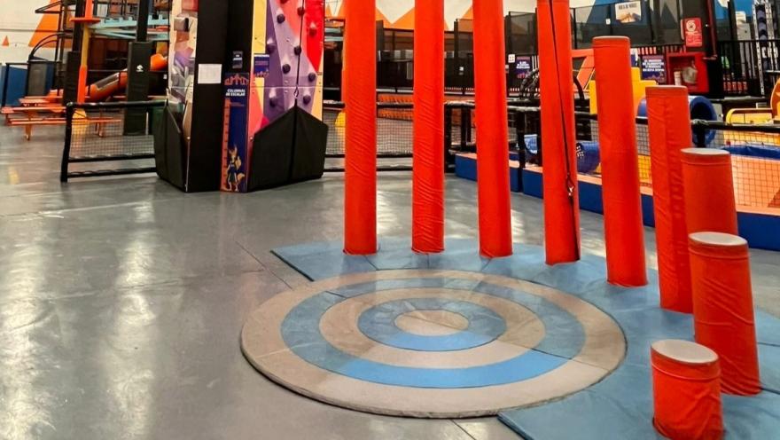 Zona de obstáculos con postes acolchados rojos y plataformas en un parque de aventura interior, diseñada para juegos de equilibrio y agilidad.
