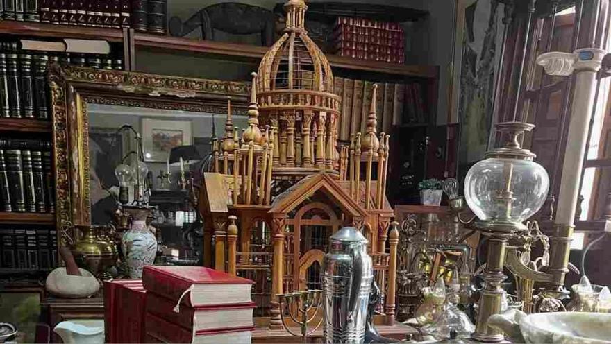 Mesa con objetos antiguos y decorativos, libros y una maqueta de madera, en una librería vintage.