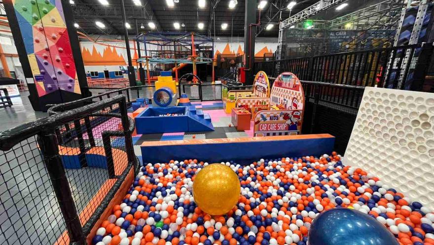 Zona de juegos infantiles en un parque interior con piscina de pelotas, estructuras coloridas y áreas de actividades para niños.
