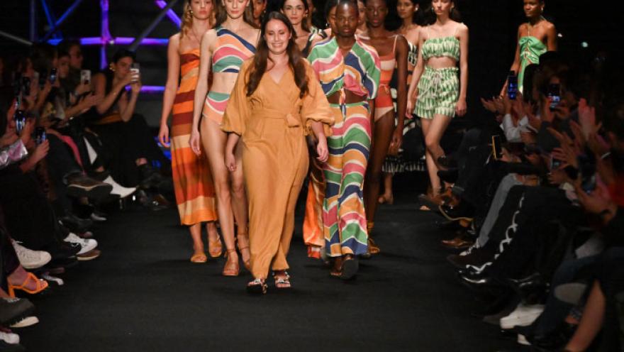Grupo de modelos desfila en pasarela con vestidos coloridos y estampados, ante público a ambos lados.