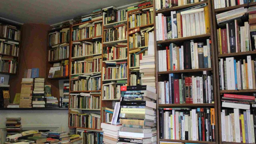 Librería repleta de estanterías altas llenas de libros y pilas apiladas en el suelo.