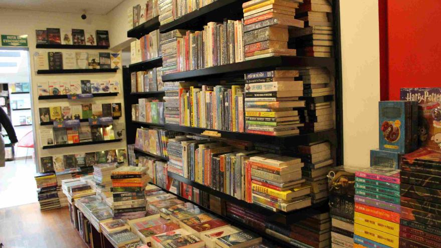 Estanterías negras llenas de libros y mesas con pilas de títulos en el interior de una librería.