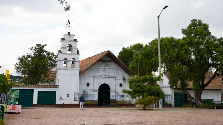 Iglesia colonial blanca con campanario en la plaza principal de Bosa, rodeada de árboles y espacio abierto.