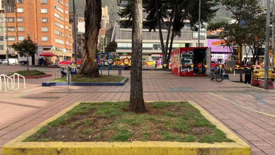 Plazoleta urbana rodeada de edificios y árboles en Bogotá, con zonas peatonales, montañas al fondo y un ambiente cotidiano de ciudad.