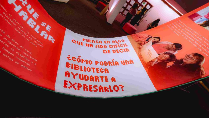 Instalación interactiva con mensajes sobre el poder de las bibliotecas y la expresión personal, exhibida en un espacio iluminado con tonos rojos y naranjas durante una muestra cultural.