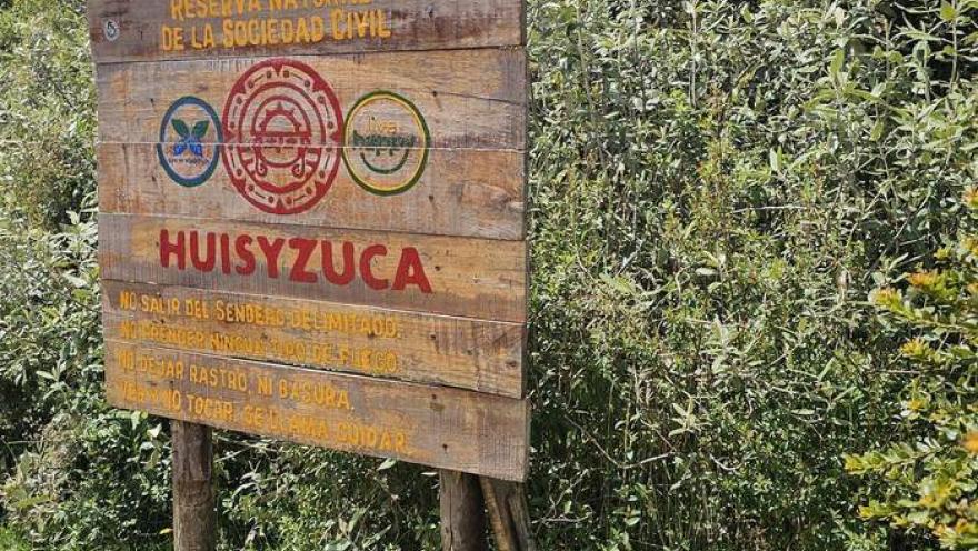 Wooden sign for the Huisyzuca Nature Reserve surrounded by vegetation in an ecological setting.