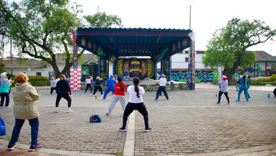 Grupo de personas realizando actividad física al aire libre frente a un escenario en la plaza de Bosa.