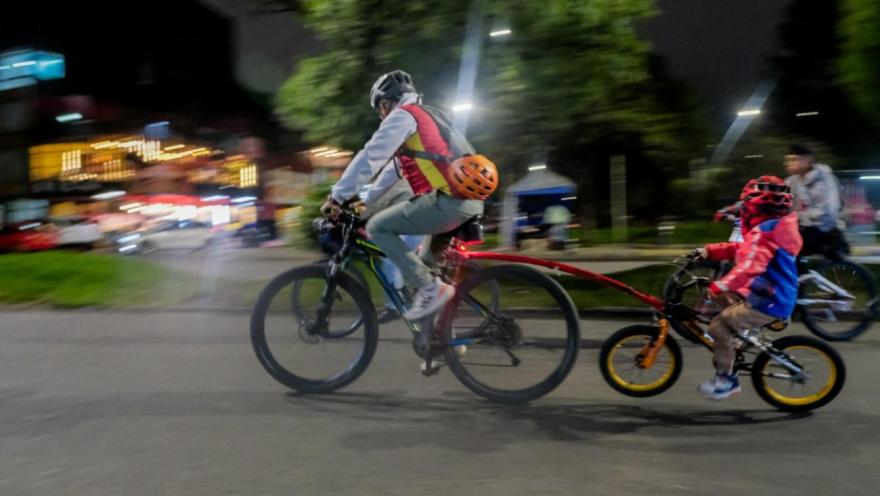Un adulto y un niño recorren en bicicleta las calles de Bogotá durante la ciclovía nocturna, una experiencia que combina deporte, familia y vida urbana bajo las luces de la ciudad.