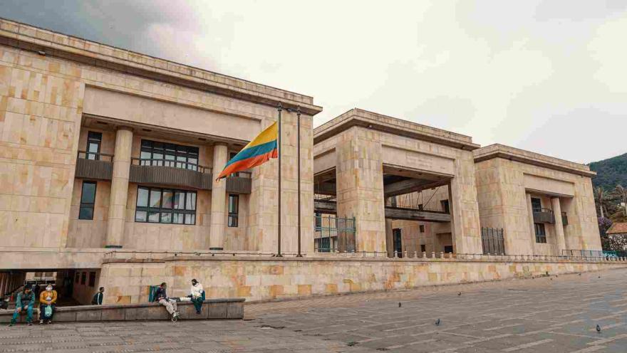 Fachada de estructura con tres edificaciones en piedra. Sobresale al frente izada una bandera de Colombia.