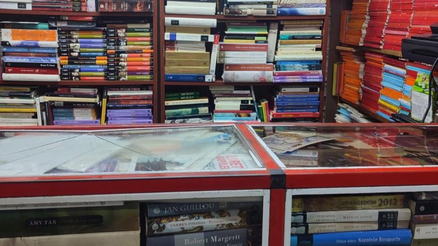 Estanterías repletas de libros y vitrinas con ejemplares exhibidos en una librería, organizados por categorías y colores.