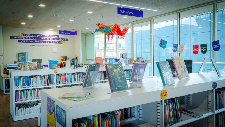  Sala infantil de biblioteca con libros exhibidos, estanterías organizadas y decoración colorida, en un espacio luminoso que invita a la lectura.