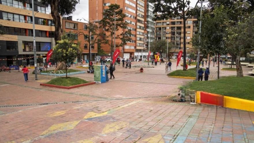 Plazoleta peatonal en Chapinero con zonas verdes, árboles y personas transitando entre edificios residenciales y comerciales de Bogotá.