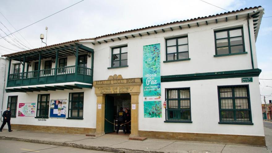  Edificio blanco de la Alcaldía Local de Bosa, con balcones verdes y personas en la entrada.
