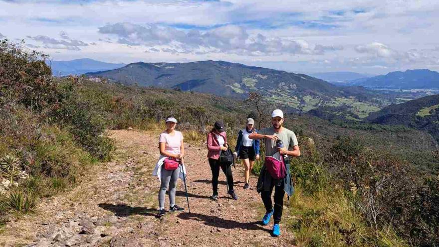 People taking an ecological hike along a mountain trail with natural landscapes and a clear sky.