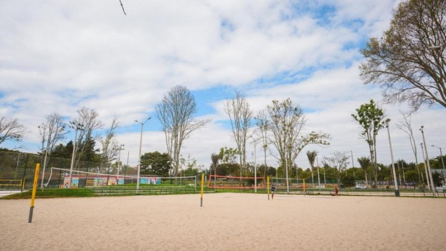 Una cancha de vóley playa se extiende en medio de un entorno natural y abierto, rodeada de árboles y zonas recreativas.