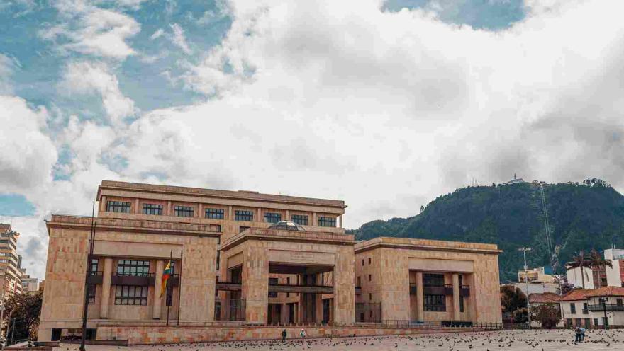 De frente, fachada de estructura con tres edificaciones en piedra. Sobresalen al fondo los cerros orientales de Bogotá.