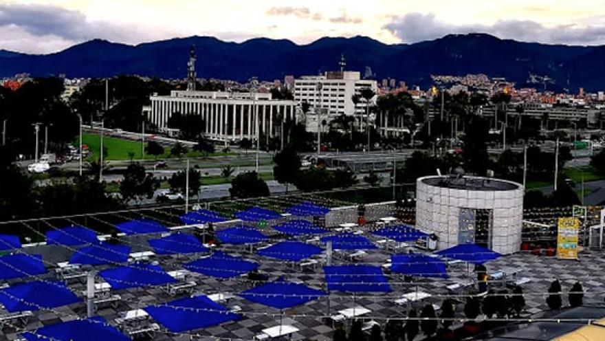 Vista panorámica de Bogotá al atardecer, con montañas al fondo y una terraza urbana con sombrillas azules en primer plano.