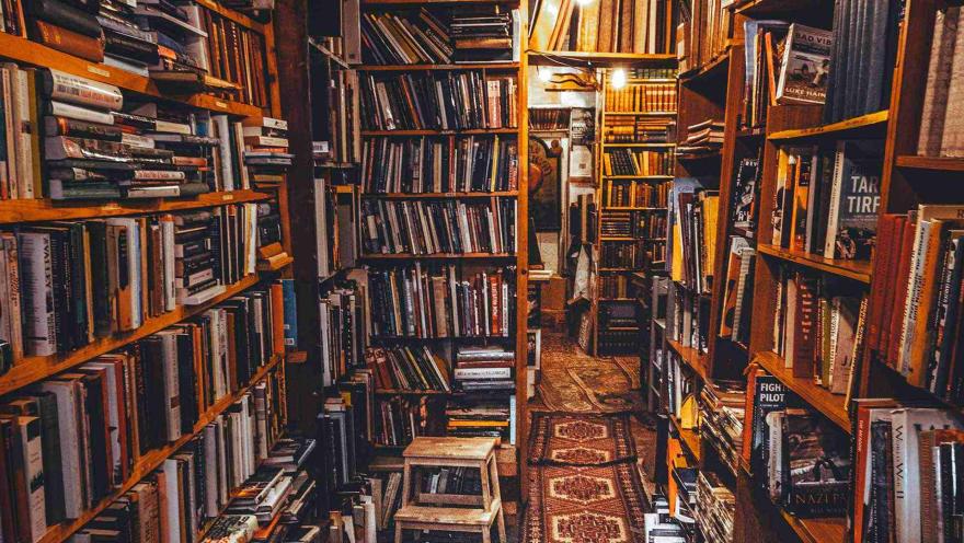 Pasillo estrecho de librería con estanterías repletas de libros y luz cálida que crea un ambiente acogedor.