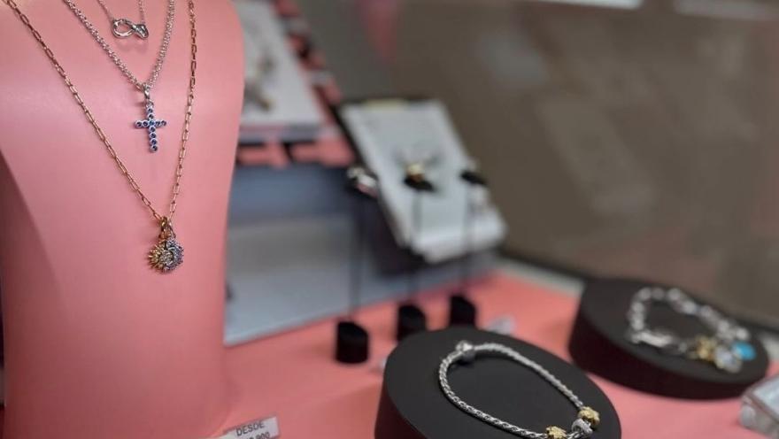  Exhibición de joyería con collares y pulseras sobre soportes rosados y negros en una vitrina de tienda.