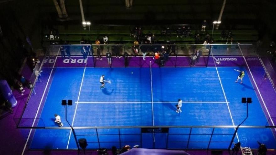 Vista aérea de una cancha de pádel durante un partido en desarrollo, donde los jugadores compiten en un escenario moderno iluminado y rodeado de graderías.