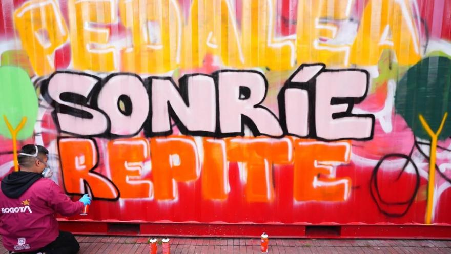 Persona realiza un grafiti con el mensaje “Pedalea, sonríe, repite” sobre un contenedor urbano en Bogotá.