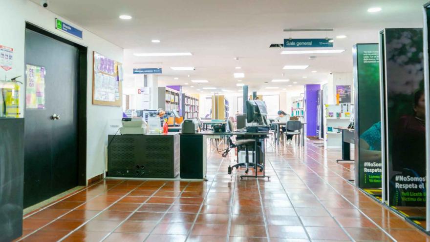Área de servicio y consulta en una biblioteca, con puestos de atención, señalización de “Sala general” y usuarios trabajando en un ambiente amplio y ordenado.