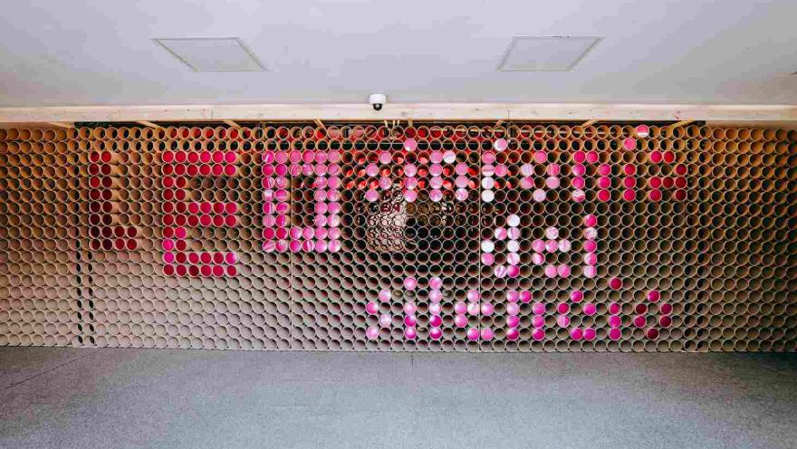  Instalación artística elaborada con tubos de cartón y elementos en tonos rosados que forman la frase “León de libros”, en un espacio cultural de exhibición.