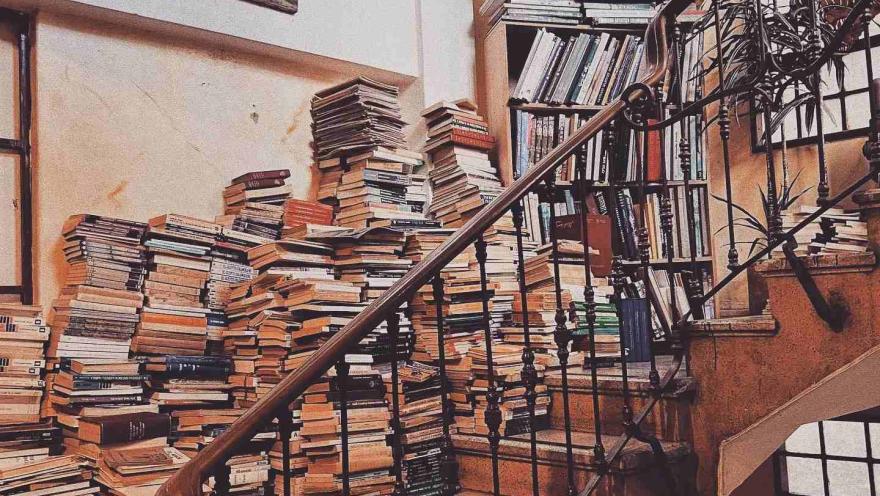  Escalera interior rodeada de estanterías y numerosas pilas de libros, en un ambiente cálido y acogedor de librería.