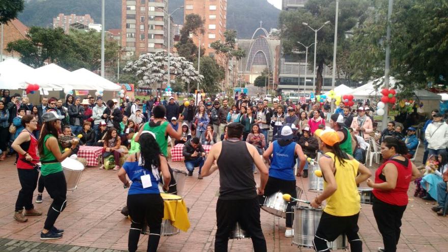 Grupo musical toca tambores en una plazoleta de Bogotá mientras decenas de personas disfrutan de una actividad cultural al aire libre.