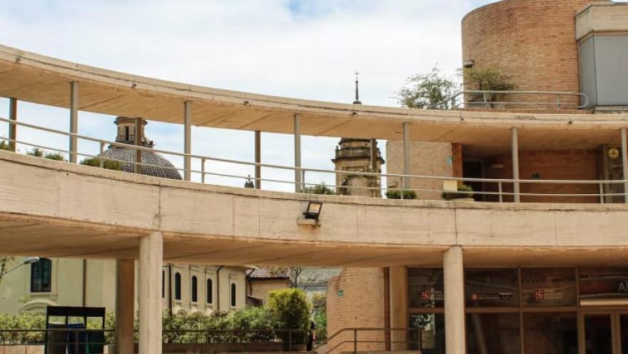 Vista del Centro Cultural Gabriel García Márquez en Bogotá, con sus característicos corredores curvos de concreto y ladrillo diseñados por Rogelio Salmona. Al fondo se observan elementos arquitectónicos del centro histórico de La Candelaria bajo un cielo parcialmente nublado.