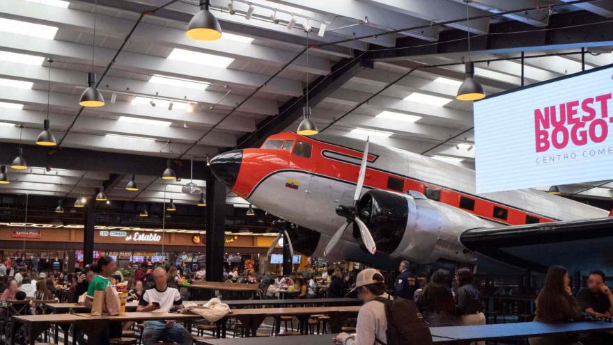 Interior del centro comercial Nuestro Bogotá con una plaza de comidas y un avión antiguo exhibido como atractivo central.