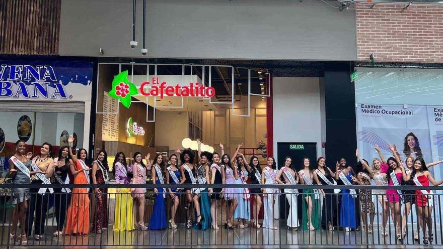  Grupo de participantes de un certamen posa en el interior de un centro comercial, vestidos con trajes elegantes y bandas de representación.