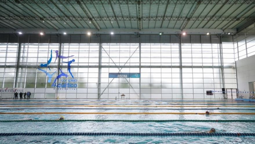  Vista interior del Complejo Acuático de Bogotá, con una amplia piscina de competición de múltiples carriles donde nadadores entrenan bajo una moderna estructura cubierta e iluminada con luz natural.