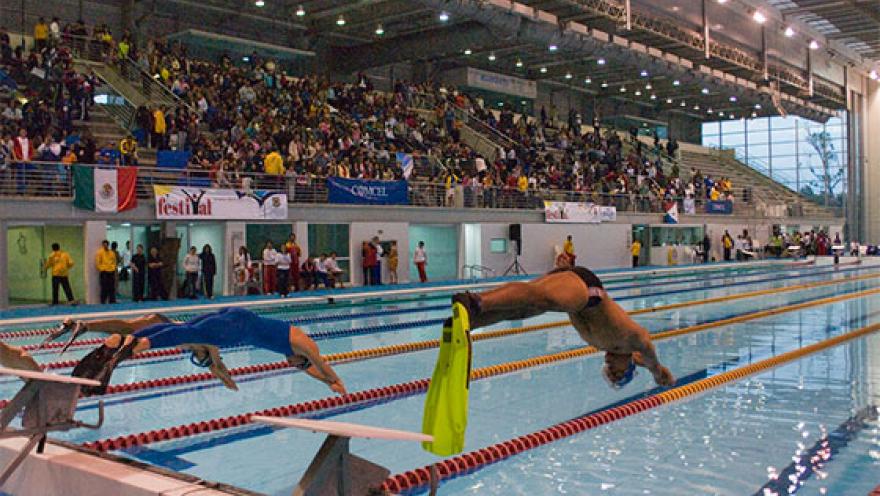 Nadadores se lanzan desde los bloques de salida durante una competencia en el Complejo Acuático de Bogotá, ante la mirada de cientos de espectadores que llenan las graderías de este escenario deportivo de nivel internacional.