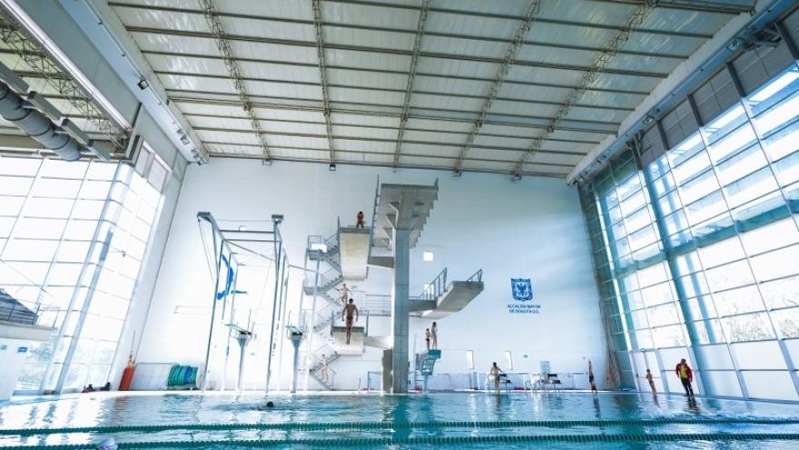 Vista interior del Complejo Acuático de Bogotá con piscina cubierta y plataforma de clavados de varios niveles, un escenario de alto rendimiento diseñado para la práctica y competencia de deportes acuáticos.