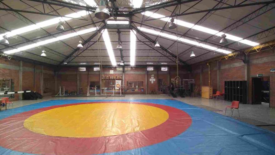 Área de entrenamiento de lucha olímpica del Coliseo Cayetano Cañizares, equipada con un amplio tapete reglamentario y espacios especializados para la preparación, formación y competencia de deportistas en disciplinas de combate.