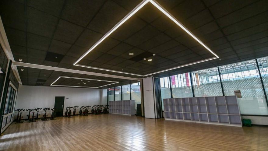 Salón multifuncional del Centro Felicidad (CEFE) El Tunal, diseñado para actividades deportivas y recreativas. El espacio destaca por su amplitud, piso de madera, iluminación moderna y ventanales que permiten la entrada de luz natural, ofreciendo un ambiente cómodo para clases grupales y entrenamiento físico.