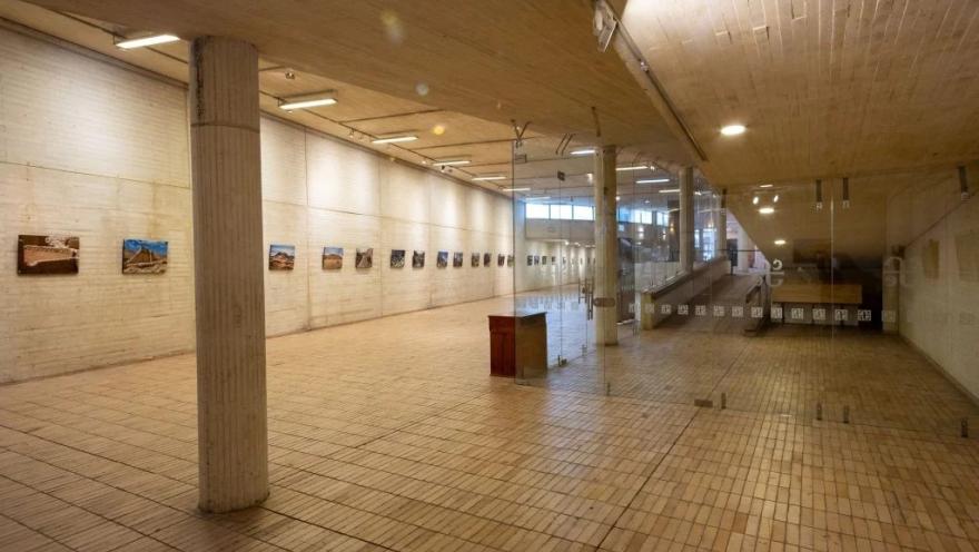 Sala de exposiciones Débora Arango del Centro Cultural Gabriel García Márquez, un amplio espacio interior con pisos y muros de ladrillo claro, columnas de concreto y una muestra fotográfica exhibida a lo largo de las paredes. El lugar está diseñado para albergar exposiciones temporales de arte y cultura.